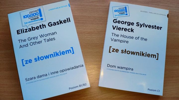 Zdjęcie przedstawia dwie książki, które podarowało wydawnictwo. Mają białe okładki i czarno-niebieskie napisy. Leżą na drewnianym blacie.